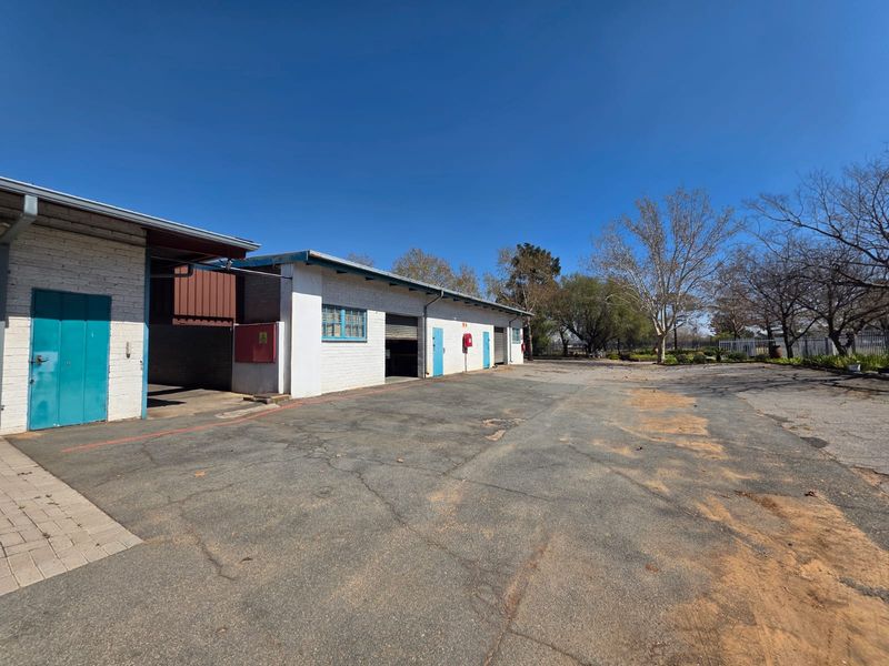 Rear exterior view of a commercial property featuring a large asphalt yard, multiple roller shutter access points, and painted brick building facade.