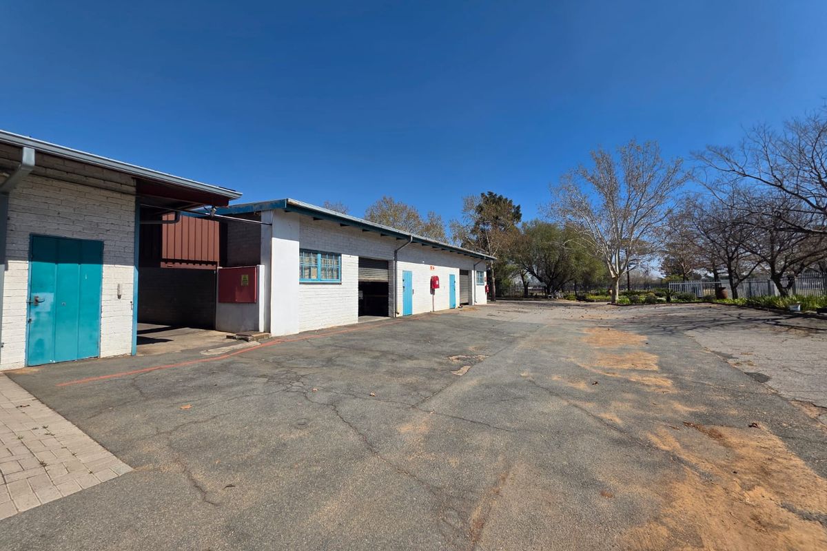 Rear exterior view of a commercial property featuring a large asphalt yard, multiple roller shutter access points, and painted brick building facade.