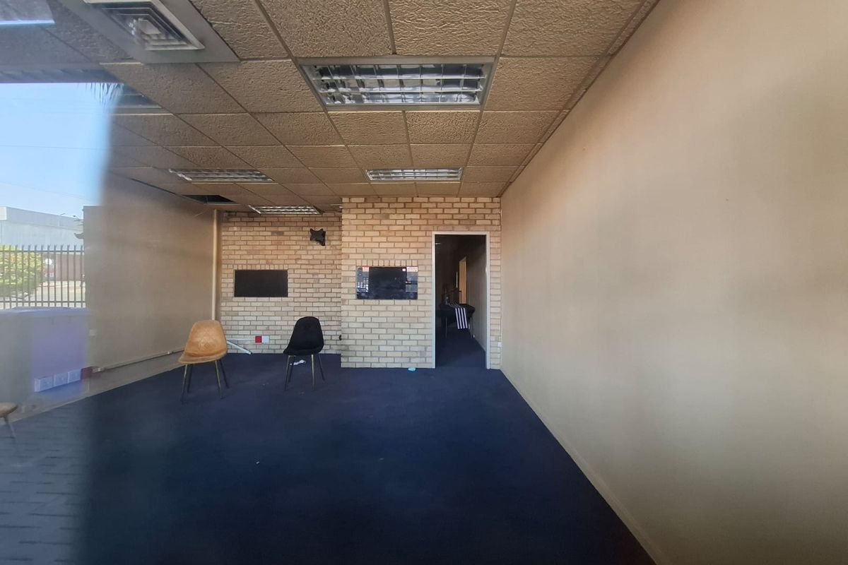 An empty, open-plan interior space featuring a suspended ceiling, exposed brick wall, and carpet flooring, suitable for various commercial or residential uses.