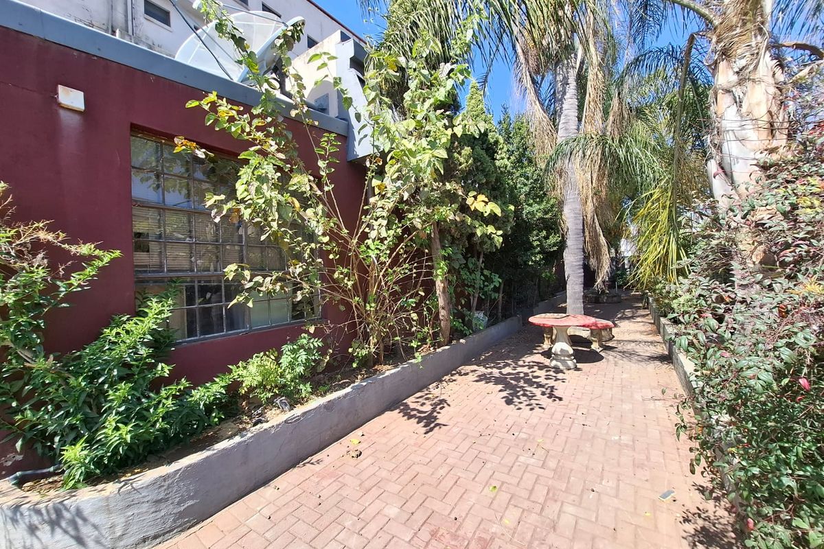 A rear exterior view of the apartment building featuring brick paving, a retaining wall, and established garden landscaping.