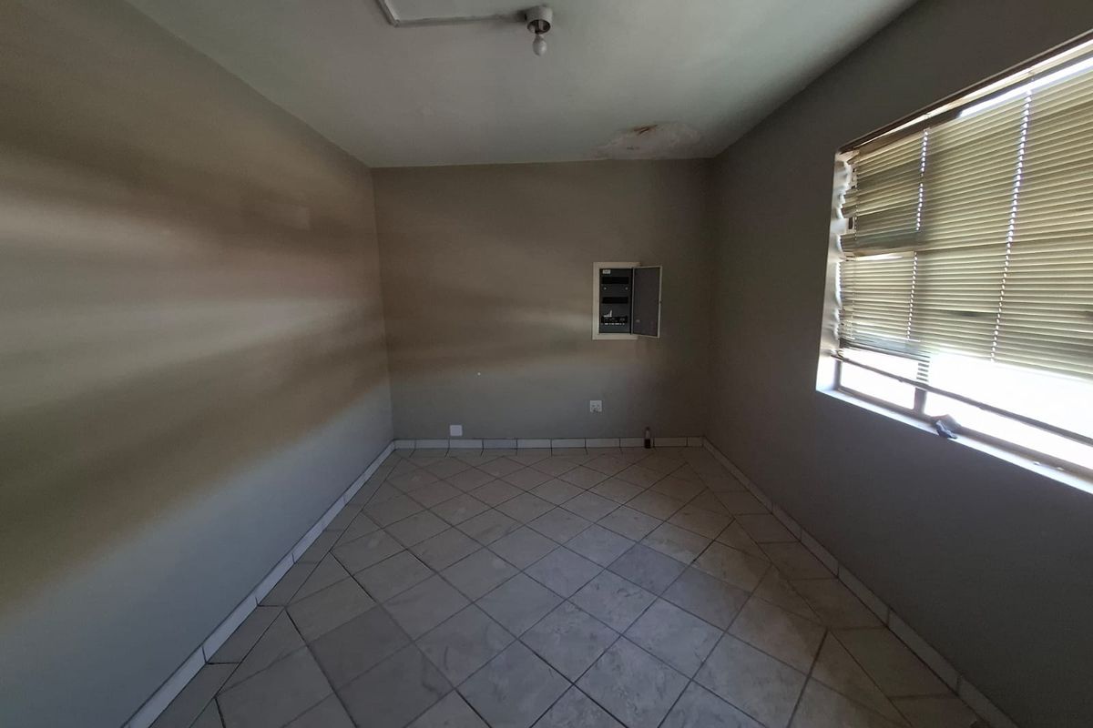 An empty bedroom featuring tiled flooring, an integrated electrical distribution board, and a window with damaged venetian blinds.