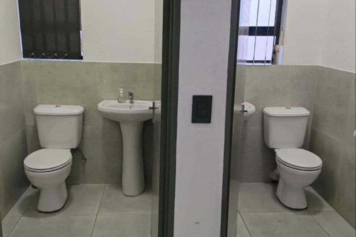 Two separate, clean office restrooms featuring modern tiled finishes, pedestal washbasins, and secure window installations.