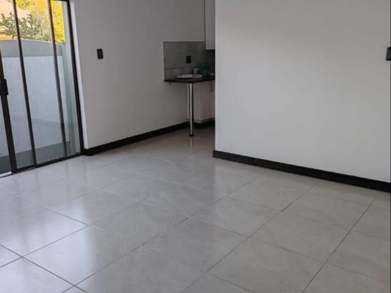 An open-plan office space featuring neutral tiled flooring, a small kitchenette area, and a sliding glass door providing access to the exterior.