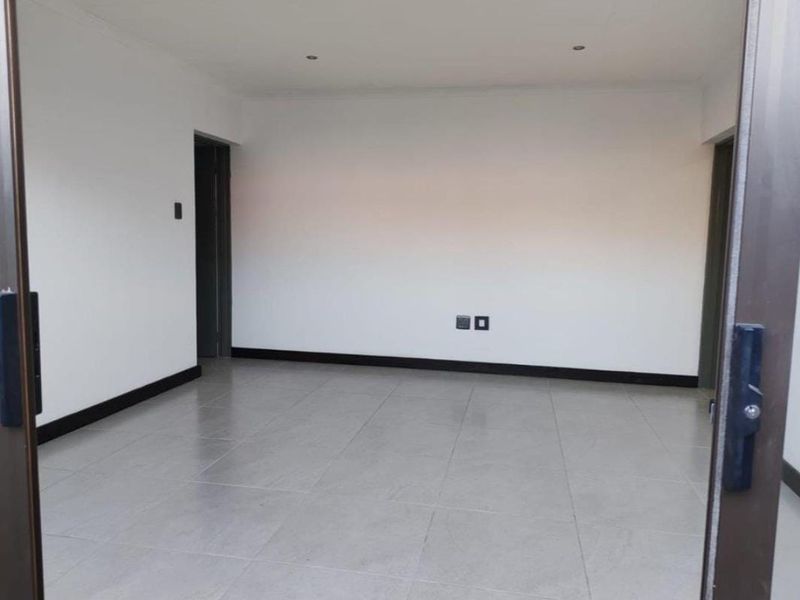 A bright, empty office space featuring neutral tiled flooring, recessed downlights, and clean white walls, ready for professional fit-out.