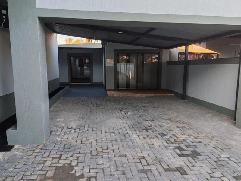 A well-maintained office exterior featuring a paved driveway, covered carport area, and a modern sliding glass door entrance.