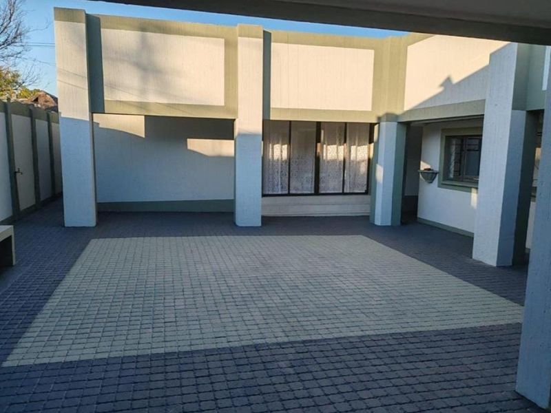 A clean, paved rear courtyard area featuring a covered patio space with structural concrete pillars and exterior wall lighting.