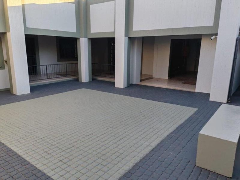 A paved courtyard area featuring concrete structural pillars, metal railings, and a security camera, providing access to the office building interior.