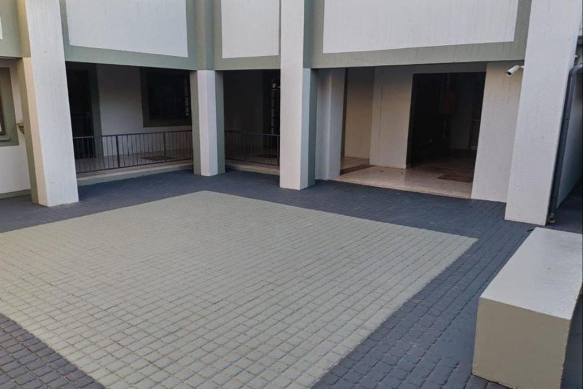 A paved courtyard area featuring concrete structural pillars, metal railings, and a security camera, providing access to the office building interior.