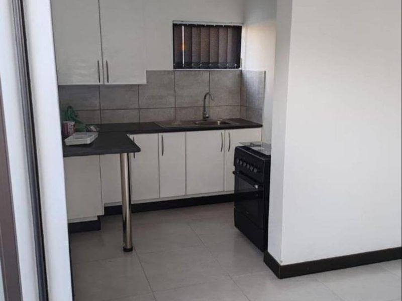 A compact, functional kitchen featuring white cabinetry, dark countertops, tiled backsplash, and a freestanding stove, presented in a clean, neutral space.