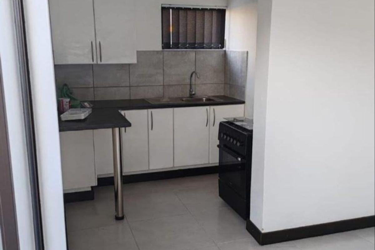 A compact, functional kitchen featuring white cabinetry, dark countertops, tiled backsplash, and a freestanding stove, presented in a clean, neutral space.