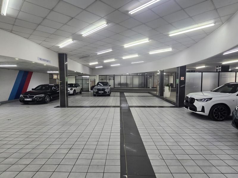 A spacious, well-lit commercial garage or delivery bay featuring tiled flooring, a suspended ceiling, and structural support columns.