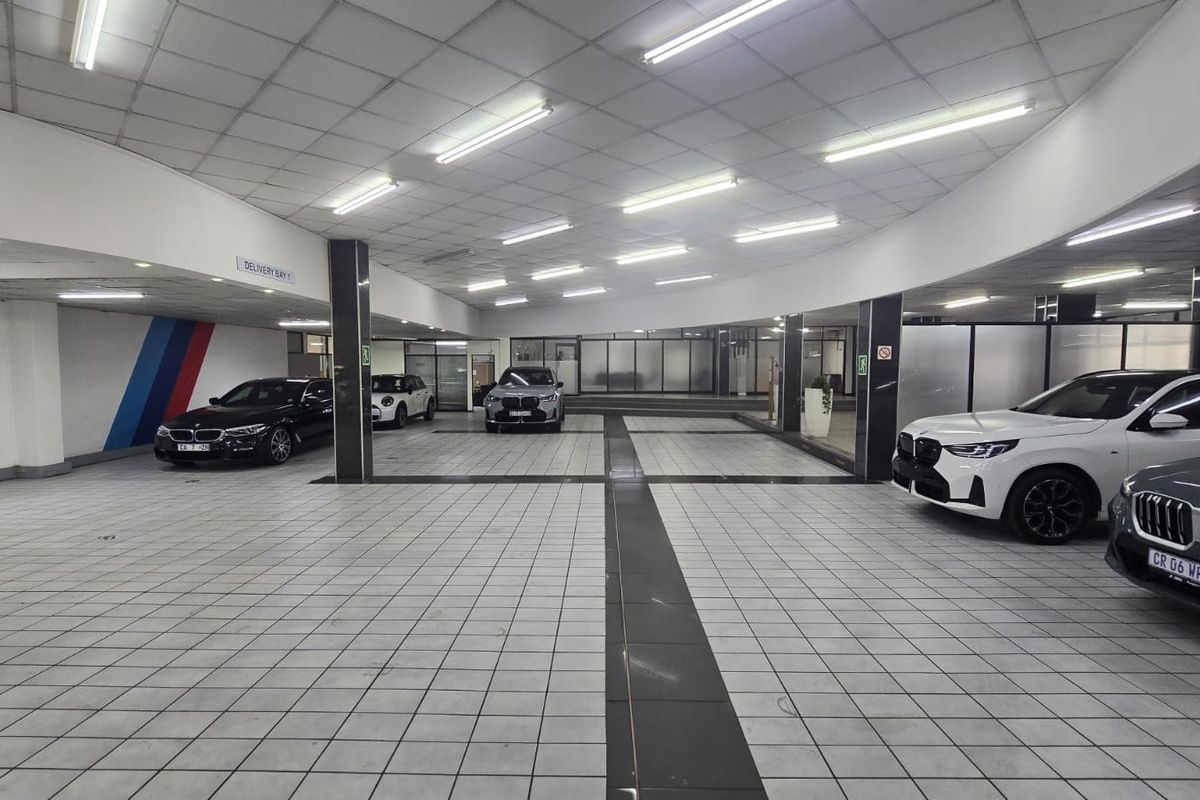 A spacious, well-lit commercial garage or delivery bay featuring tiled flooring, a suspended ceiling, and structural support columns.
