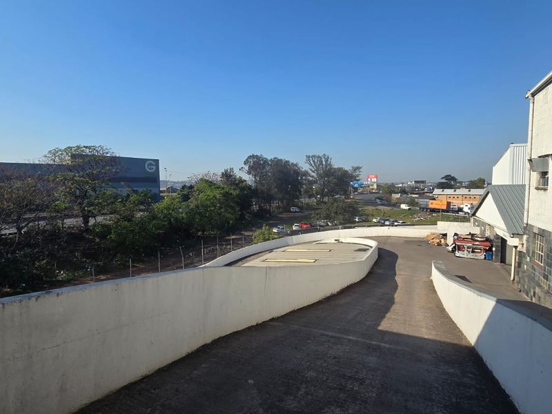 An elevated view of a concrete vehicle ramp leading to the rear of a commercial building with stone and masonry facade details.