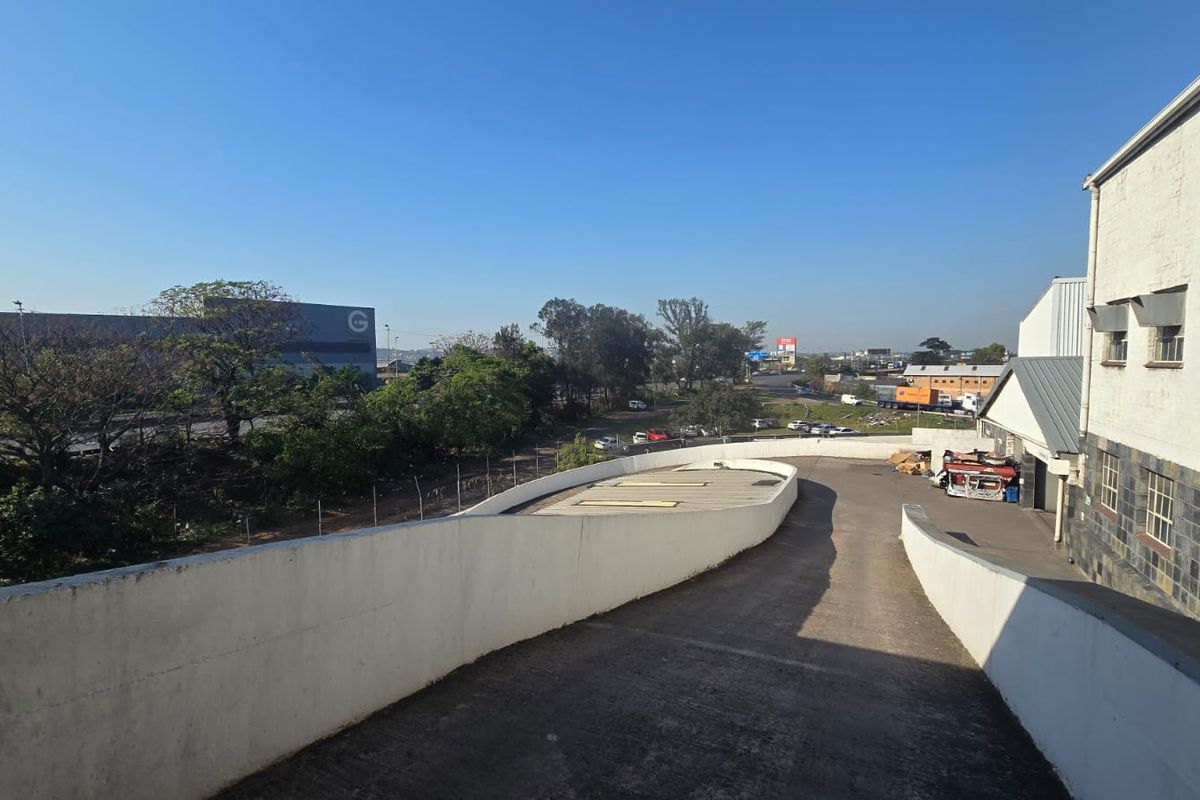 An elevated view of a concrete vehicle ramp leading to the rear of a commercial building with stone and masonry facade details.