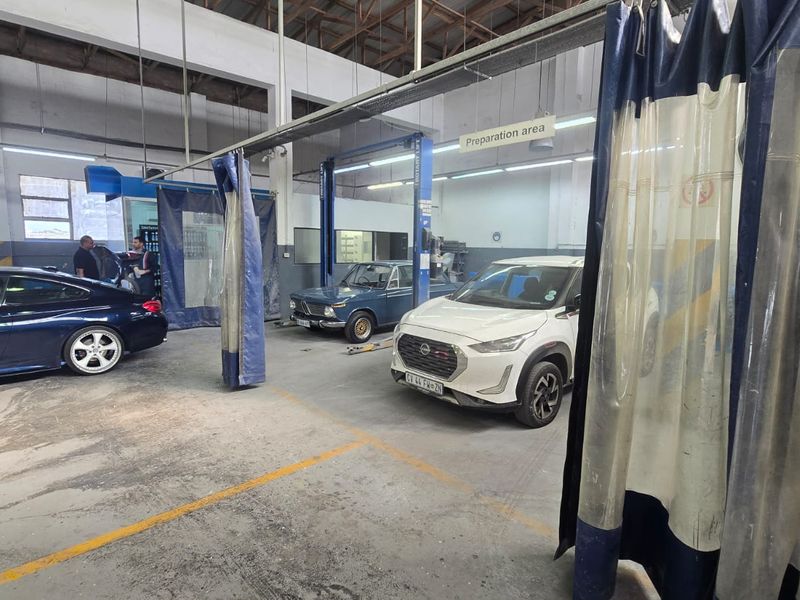 Commercial automotive workshop featuring vehicle lifts, industrial curtain partitions, and exposed steel roof structure with durable concrete flooring.