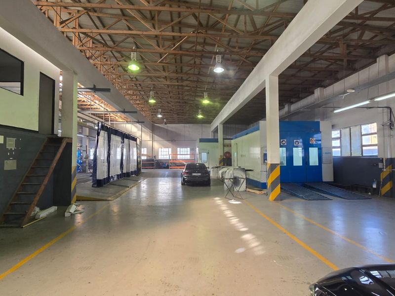 Spacious industrial workshop featuring exposed timber roof trusses, concrete flooring, and a dedicated spray booth area, suitable for automotive or commercial repair operations.