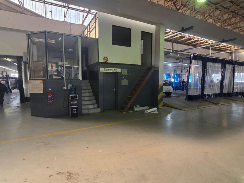 Spacious commercial workshop area featuring concrete flooring, exposed steel roof trusses, a mezzanine office structure, and industrial curtain partitions for work bays.