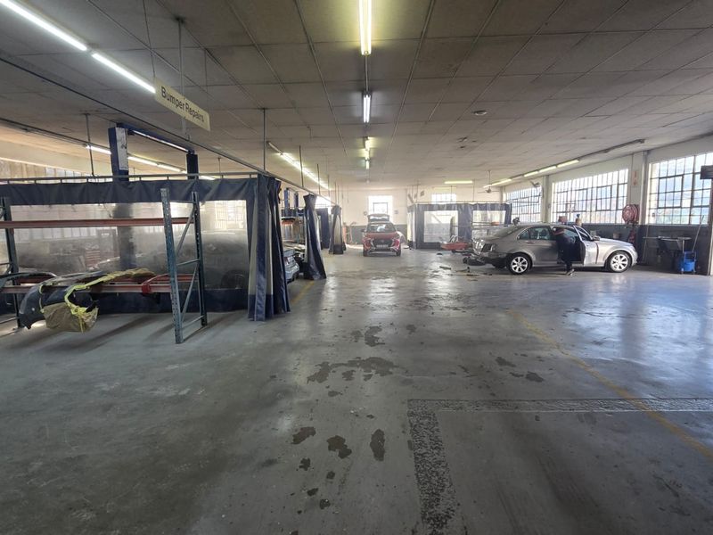 Spacious commercial garage facility featuring industrial concrete flooring, overhead fluorescent lighting, and dedicated spray booth areas with partitioned curtains.