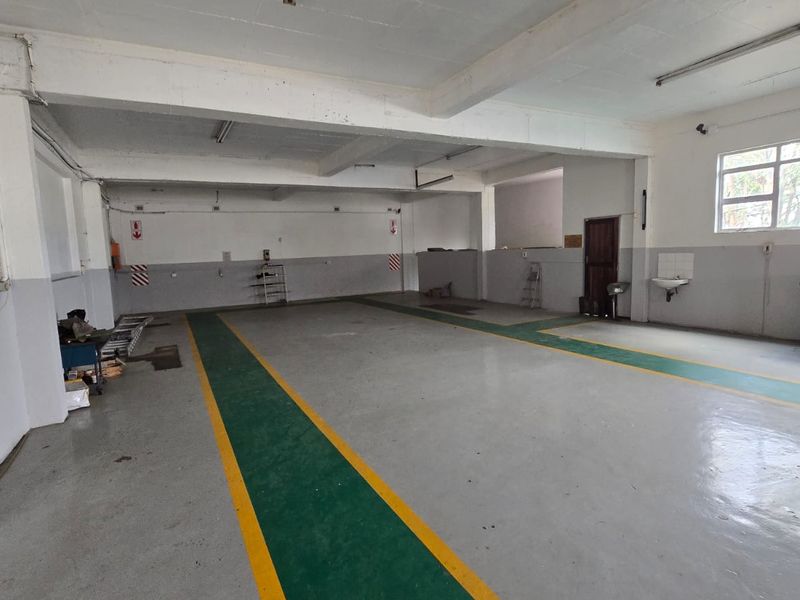 Spacious commercial garage or workshop area featuring painted concrete flooring, exposed structural beams, and a wall-mounted basin.