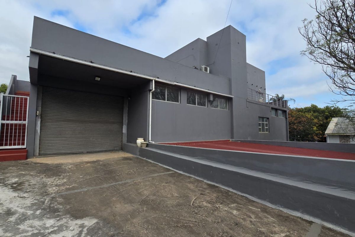 Rear exterior view of a commercial building featuring a large roller shutter door, concrete ramp access, and external staircase.