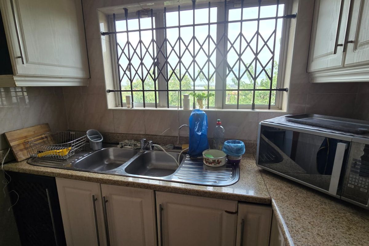 A functional kitchen area featuring granite countertops, a double bowl stainless steel sink, and built-in cabinetry with security bars on the window.