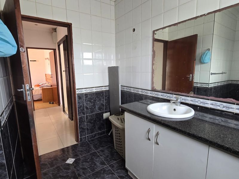 Bathroom featuring a granite-topped vanity with dual sinks, tiled walls and flooring, and a large wall-mounted mirror.