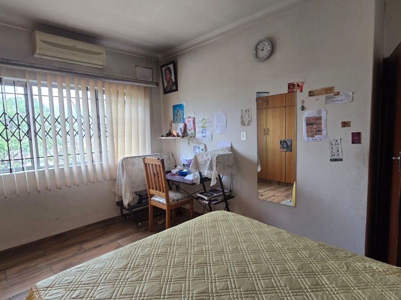 A functional bedroom featuring laminate flooring, a built-in wardrobe, and a wall-mounted air conditioning unit with security bars on the window.