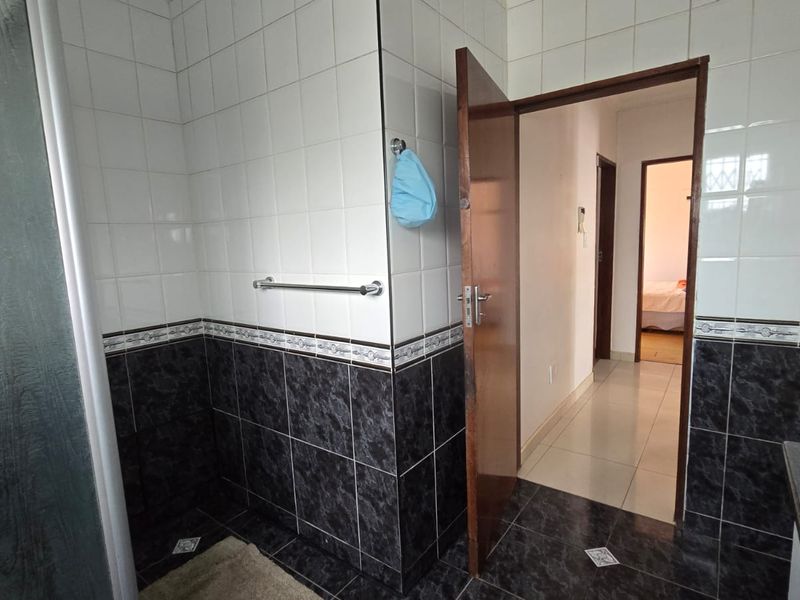 A functional bathroom featuring a shower enclosure with contrasting black and white wall tiles and tiled flooring.
