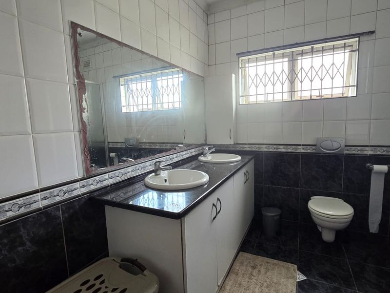 A functional bathroom featuring a double vanity with built-in cabinetry, wall-mounted toilet, and tiled finishes throughout.
