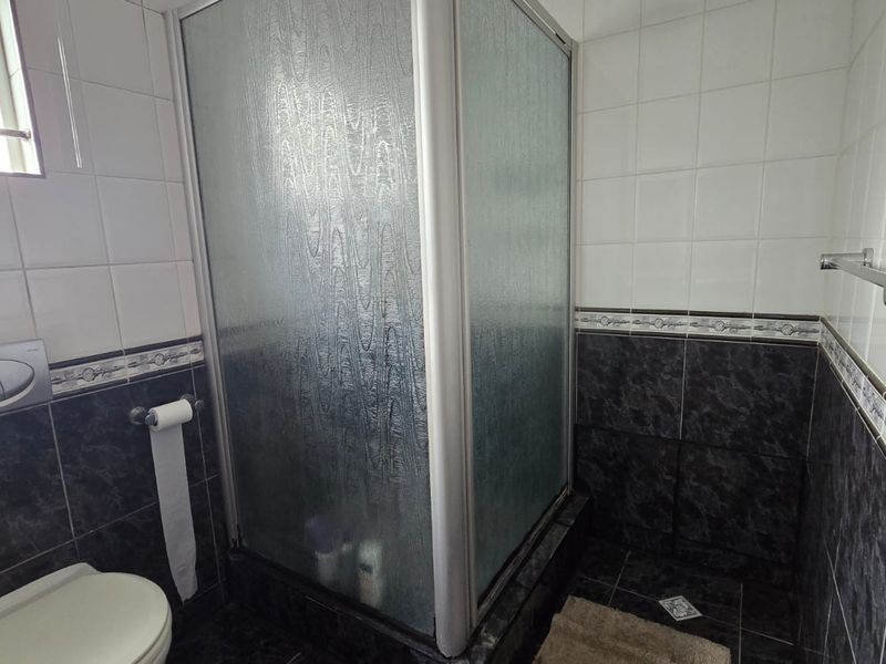 A functional bathroom featuring a corner shower enclosure, wall-mounted toilet, and contrasting dark and light tiled wall finishes.