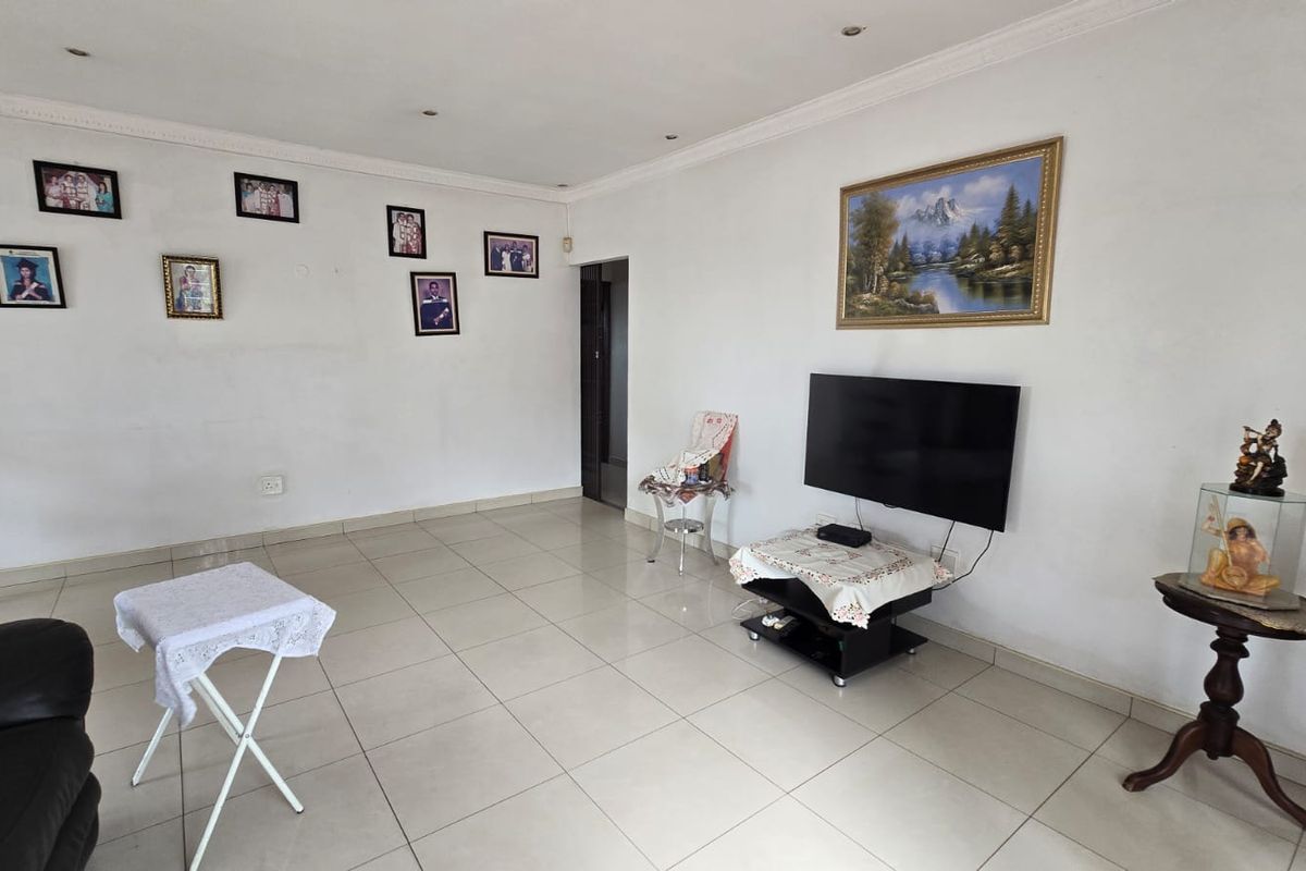 A spacious living area featuring neutral tiled flooring, recessed ceiling lighting, and decorative coving, providing a clean and functional foundation for interior design.
