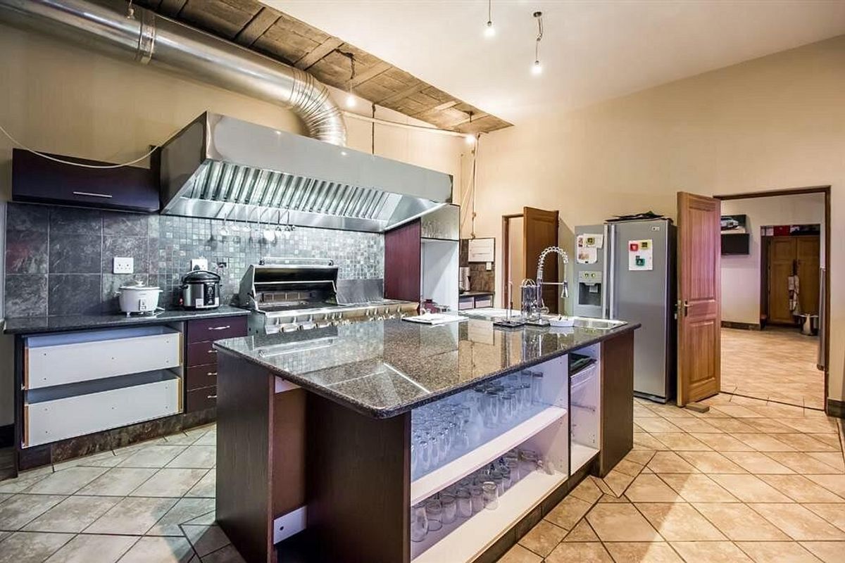 Spacious commercial-style kitchen featuring a large granite island, stainless steel extractor hood, gas range, and tiled flooring with some cabinetry requiring minor repairs.