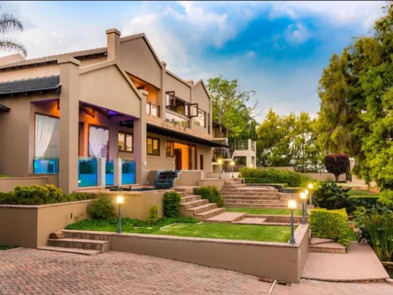 A well-maintained rear exterior view of the property featuring terraced landscaping, paved pathways, and a multi-level building structure with balcony access.