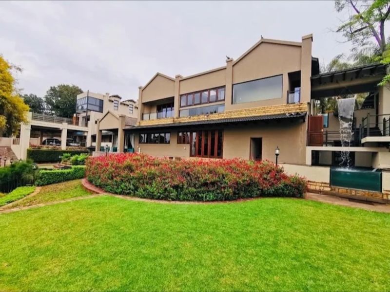 Rear view of the hotel property featuring a well-maintained lawn, landscaped garden beds, a stone water feature, and multi-level balconies.