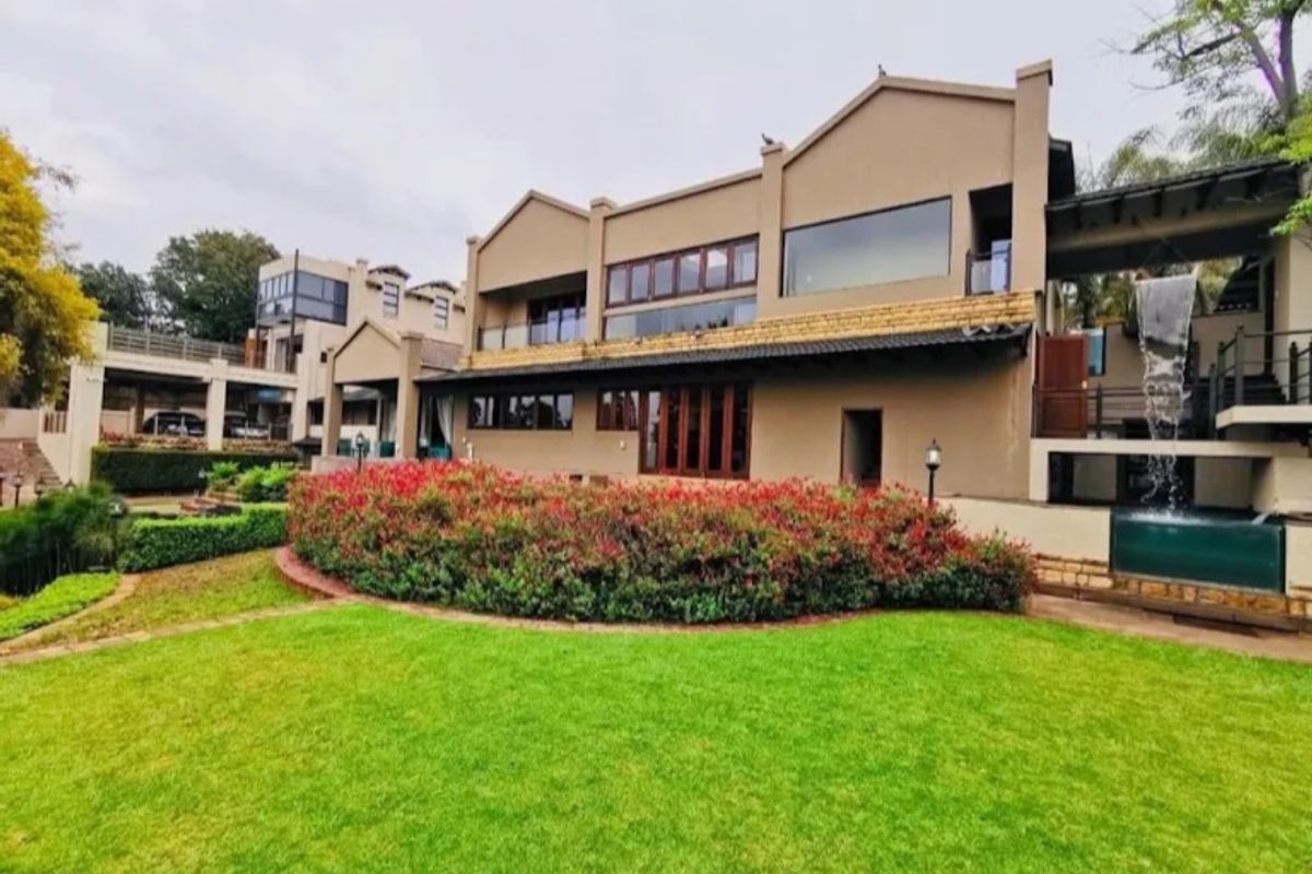 Rear view of the hotel property featuring a well-maintained lawn, landscaped garden beds, a stone water feature, and multi-level balconies.
