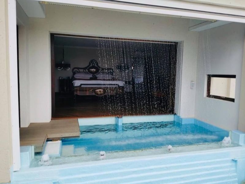 A unique hotel suite featuring a private plunge pool with an integrated water feature, seamlessly connected to the bedroom through large sliding glass doors.