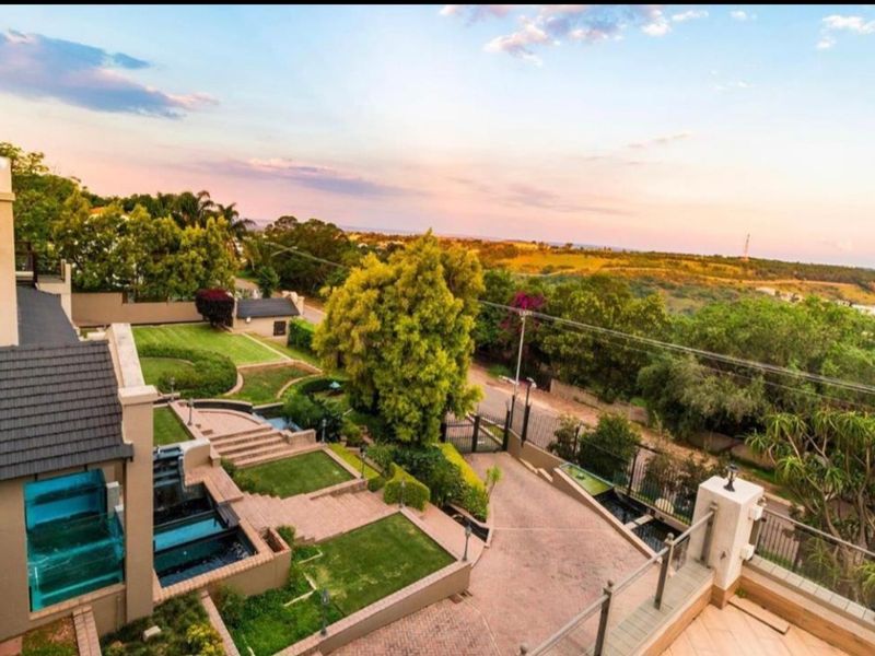 Aerial view of the property showcasing a well-maintained terraced garden, paved driveway, water features, and expansive surrounding landscape views.