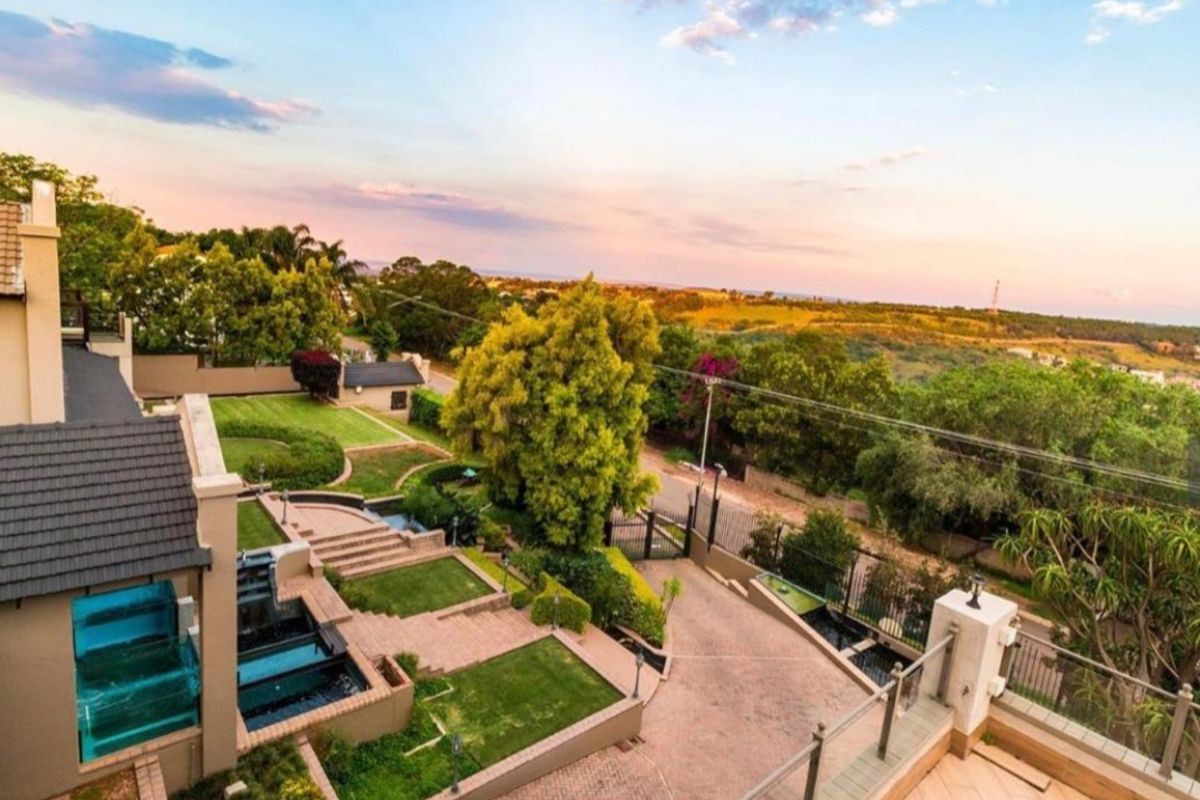Aerial view of the property showcasing a well-maintained terraced garden, paved driveway, water features, and expansive surrounding landscape views.