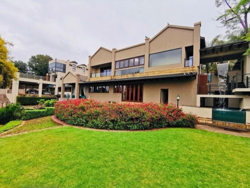 Rear view of the hotel property featuring a well-maintained lawn, landscaped garden, and a prominent water feature integrated into the building structure.