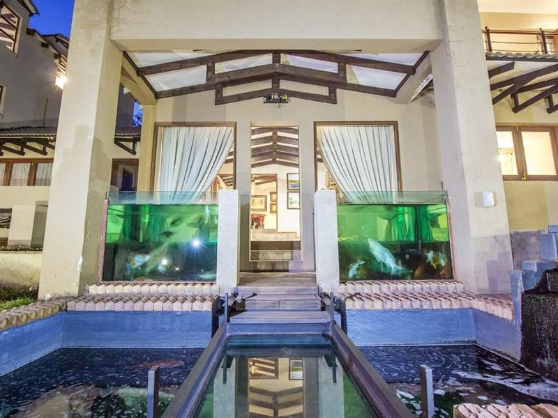 A unique rear exterior view featuring a covered patio with exposed timber beams, integrated glass fish tanks, and a central water feature with a walkway.