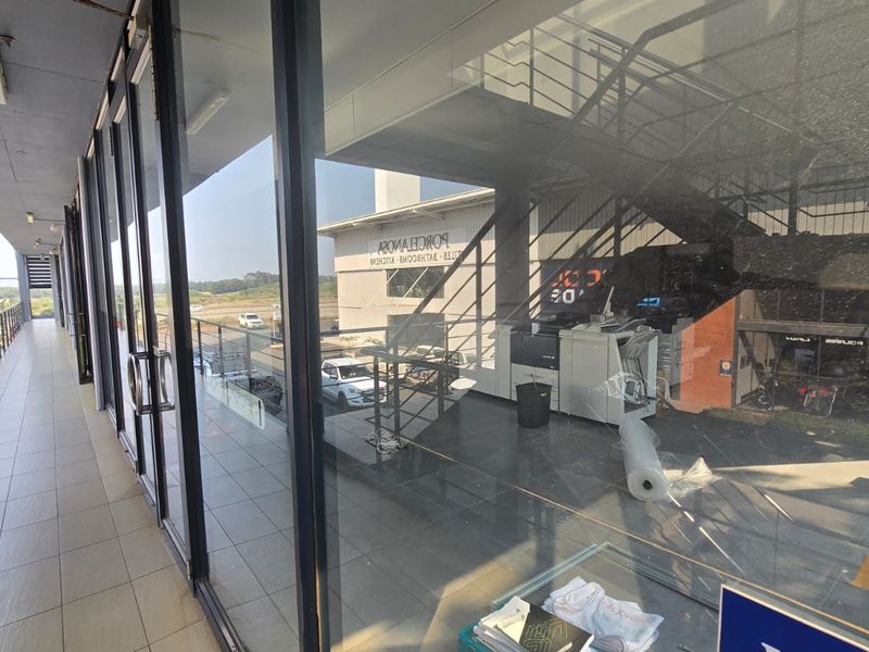 A covered balcony area with tiled flooring and extensive glass frontage, providing a view into the commercial interior space.
