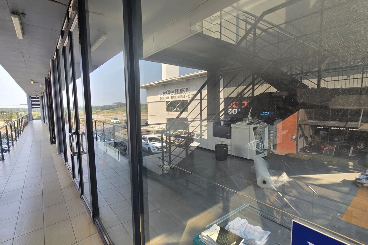 A covered balcony area with tiled flooring and extensive glass frontage, providing a view into the commercial interior space.