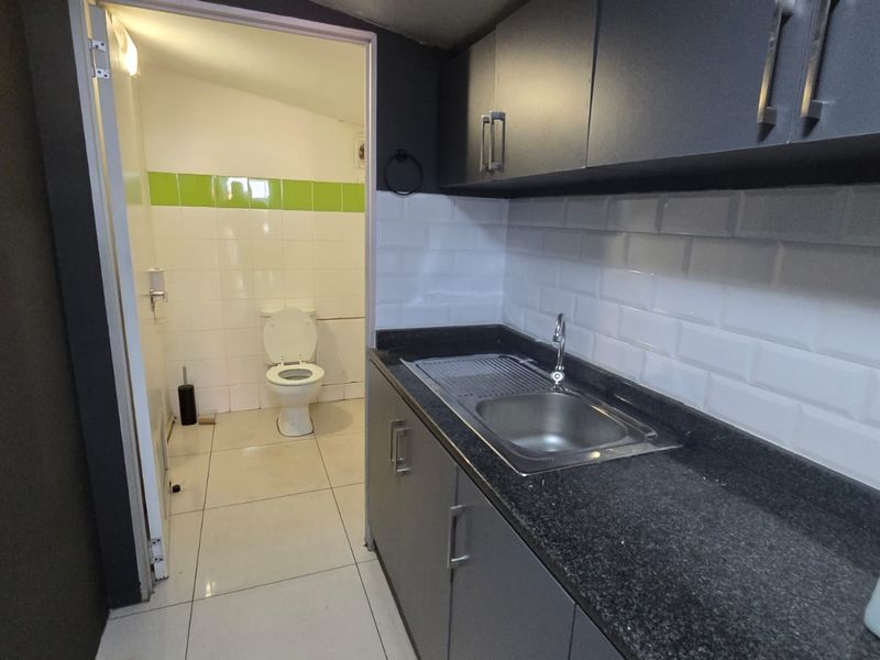 A compact kitchenette featuring dark cabinetry, granite countertops, and a subway tile backsplash, with an adjacent private restroom facility.