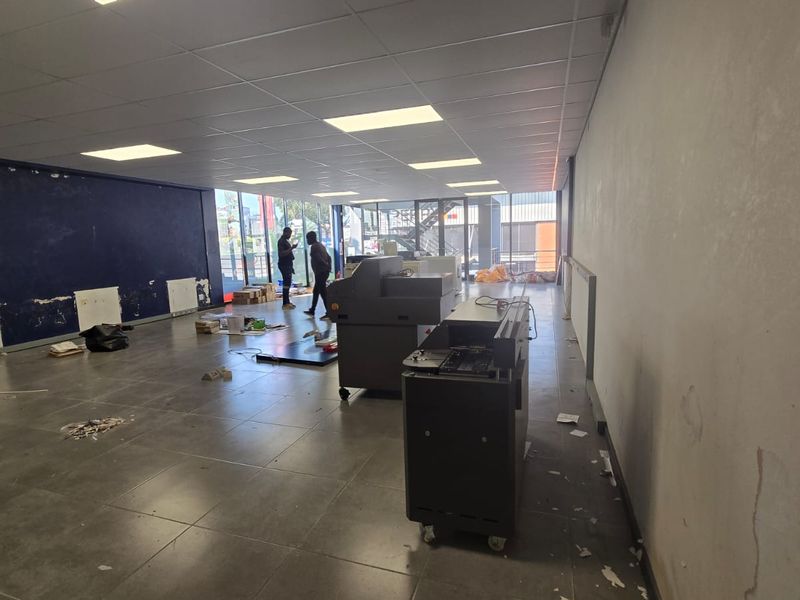 Open-plan commercial space featuring tiled flooring, suspended ceiling with recessed lighting, and large glass windows, currently requiring cosmetic wall repairs.