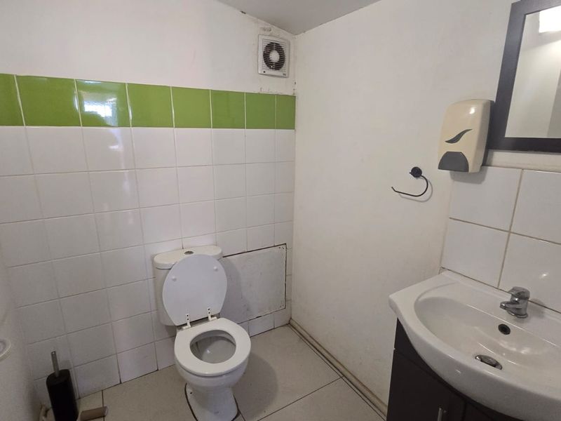 A functional commercial bathroom featuring a standard toilet, vanity basin, and partial wall tiling with an extractor fan.