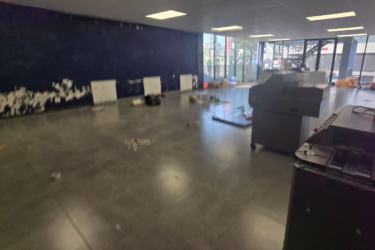 Spacious open-plan commercial area featuring large glass windows, tiled flooring, and recessed lighting, currently in need of cosmetic wall repairs.