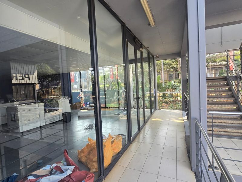 Exterior view of a commercial storefront featuring a glass facade, tiled walkway, and an adjacent metal staircase.
