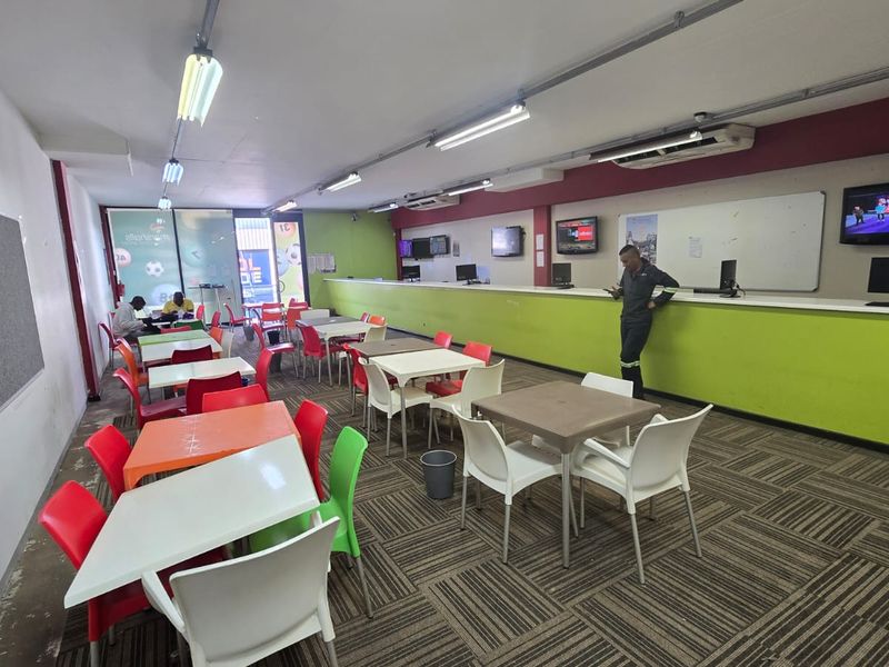 Open-plan commercial space featuring a long service counter, wall-mounted screens, whiteboard, and fluorescent lighting, suitable for a betting shop or office environment.