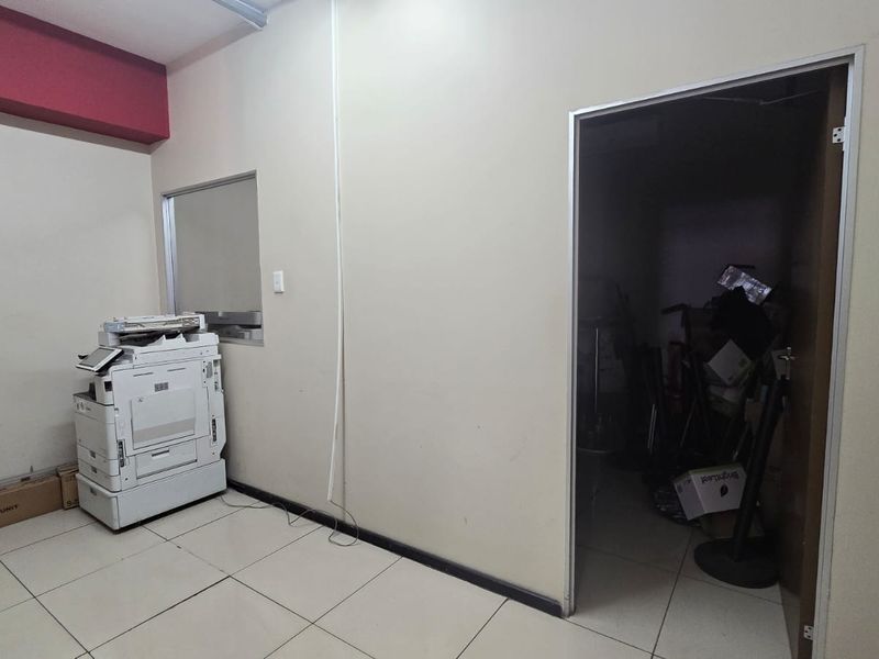 A functional office space featuring tiled flooring, an internal window, and an adjacent storage area, requiring minor cosmetic updates.