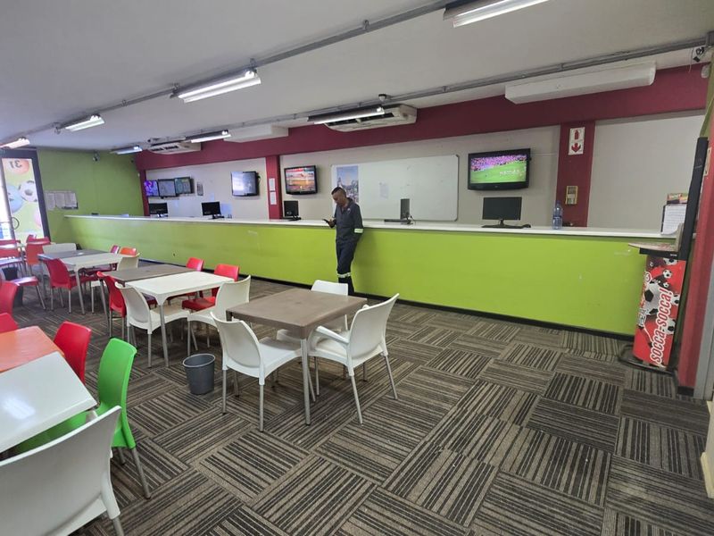 Open-plan commercial space featuring a long service counter, wall-mounted televisions, fluorescent lighting, and carpeted flooring, suitable for a betting shop or service center.